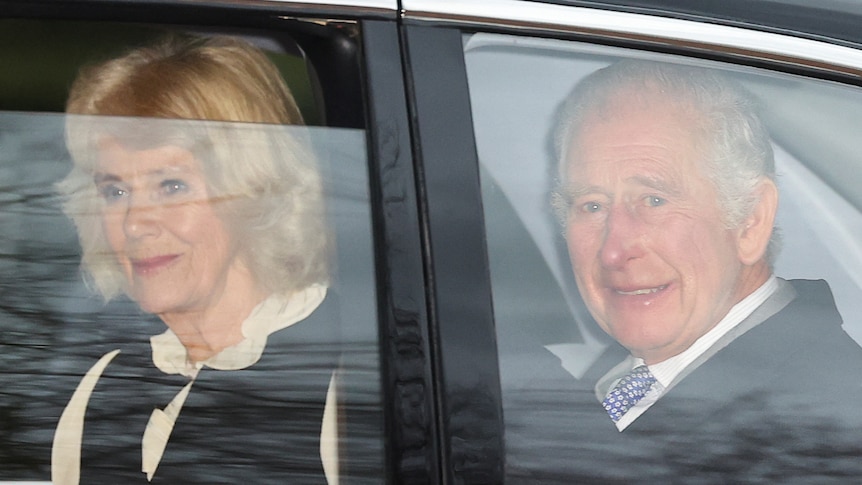 King Charles and Camilla are seen through the window of a car.