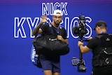 Australian tennis player Nick Kyrgios waves at the crowd as he walks in front of an electronic sign with his name on it.