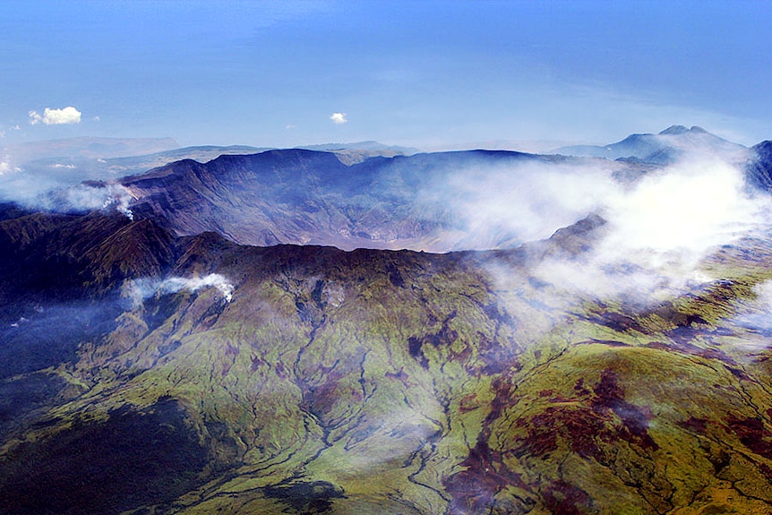 An aerial shot looking towards a massive crater-like rim on a green rocky landscape