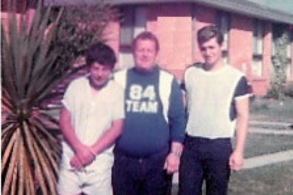 An old photo of a man and two young boys next to palm trees