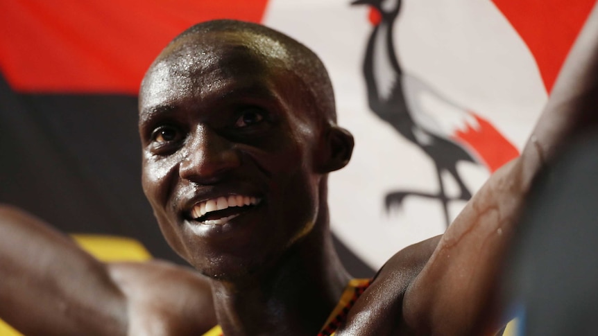 Joshua Cheptegei smiles, holding up a Uganda flag behind him