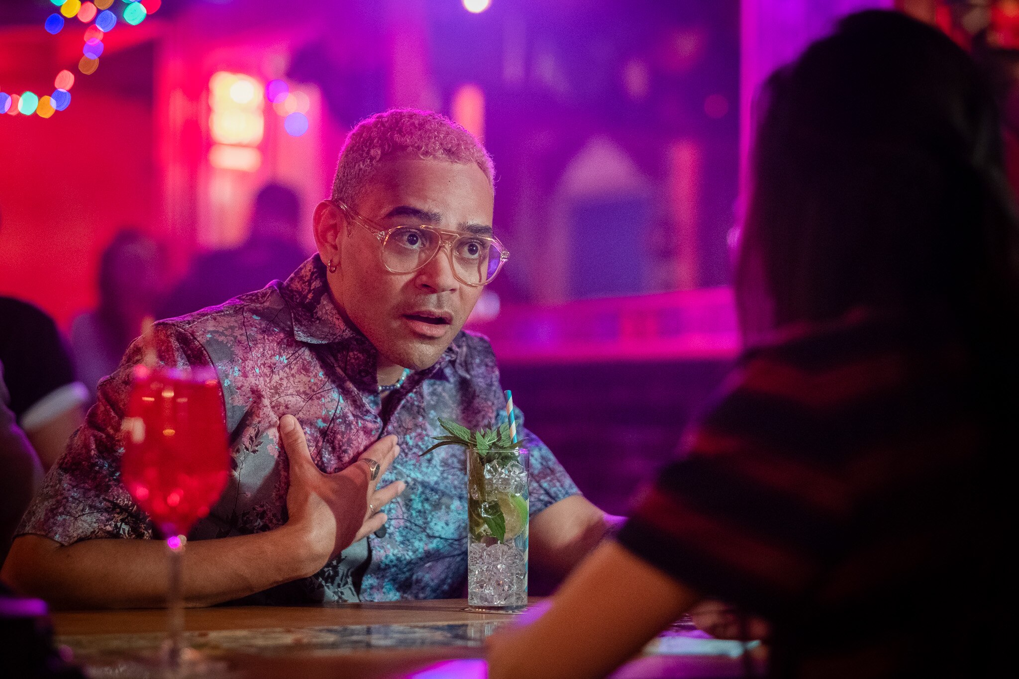 Ilai is pictured mid-conversation with a hand to his chest as he peers at his friend across a table, a drink in front of him.