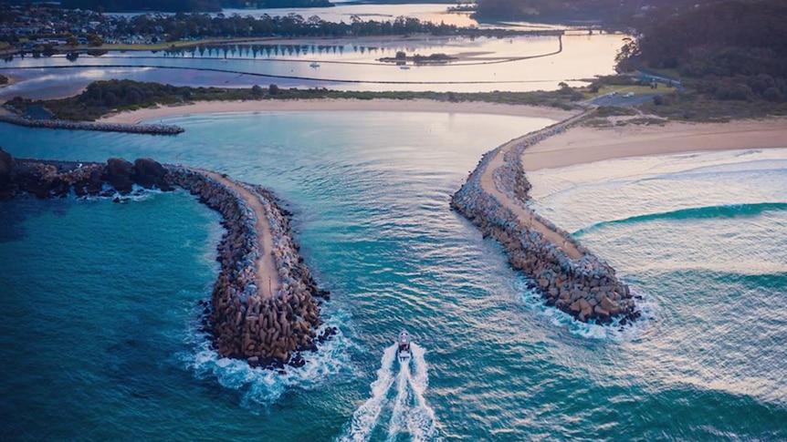 An aerial view of a boat entering the inlet between two rock walls at Narooma