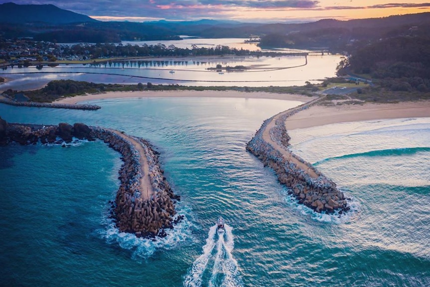 An aerial view of a boat entering the inlet between two rock walls at Narooma