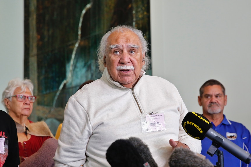 Anderson stands in front of microphones, other members of the Blak Sovereign Movement behind him.