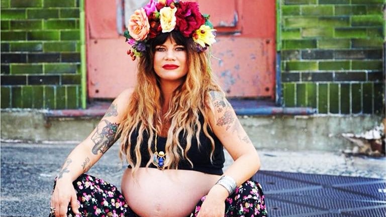 A pregnant Constance Hall wearing flower crown, sitting on step