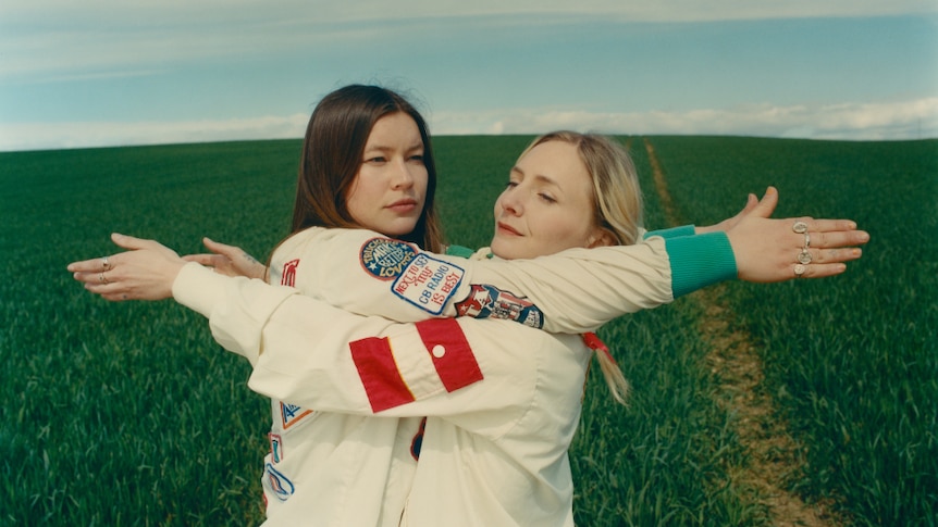 Hester and Rhian from Wet Leg stand in a field in each other's arms