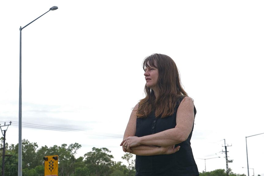 A photo of a woman standing on the side of a highway looking concerned.