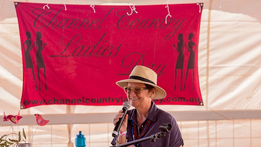 WOW Australian Executive Producer Cathy Hunt standing in front of a Channel Country Ladies Day sign, holding a microphone.