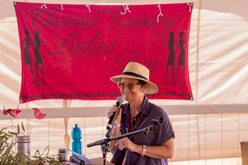 WOW Australian Executive Producer Cathy Hunt standing in front of a Channel Country Ladies Day sign, holding a microphone.