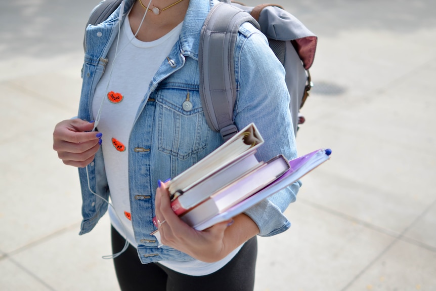 A woman holds books and carries a backpack .