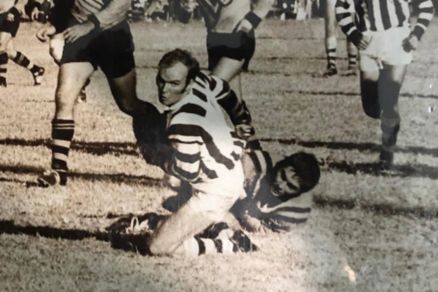 Ray Steele looks to pass the ball on his knees with players running towards him