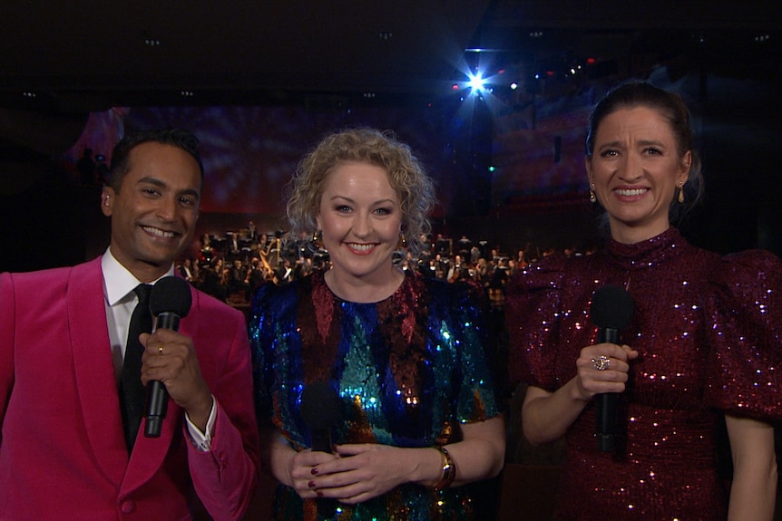 Jeremy Fernandez wearing a red suit, smiling and standing next to Zan Rowe and Genevieve Lang wearing sparkly dresses