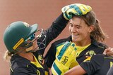 Alyssa Healy (left) rubs the head of bowler Annabel Sutherland as Rachael Haynes (back to camera) rushes in to join them.