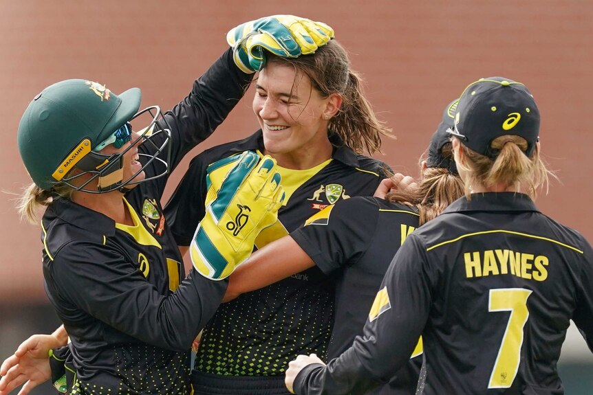 Alyssa Healy (left) rubs the head of bowler Annabel Sutherland as Rachael Haynes (back to camera) rushes in to join them.