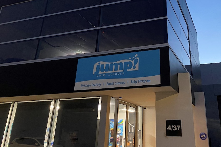 A sign on a building at dusk which says Jump swim school.