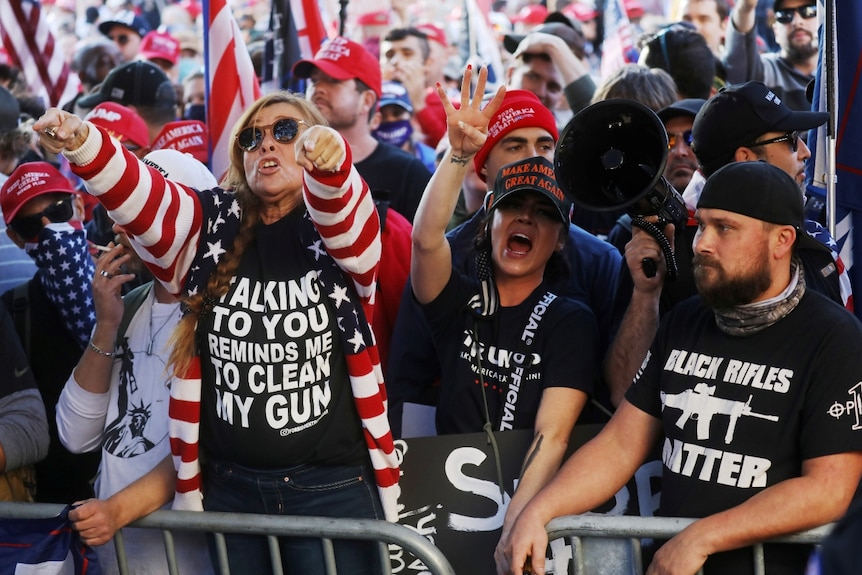 people behind a steel barrier huddle together wearing slogans on their shirts and caps