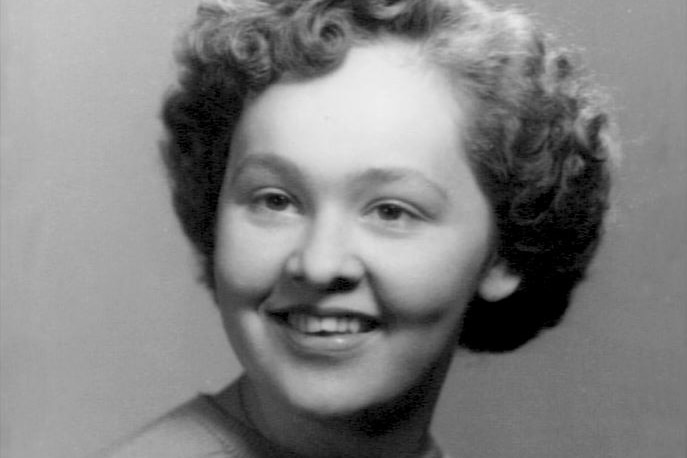 A black and white photo of a young woman with cropped curly hair, smiling
