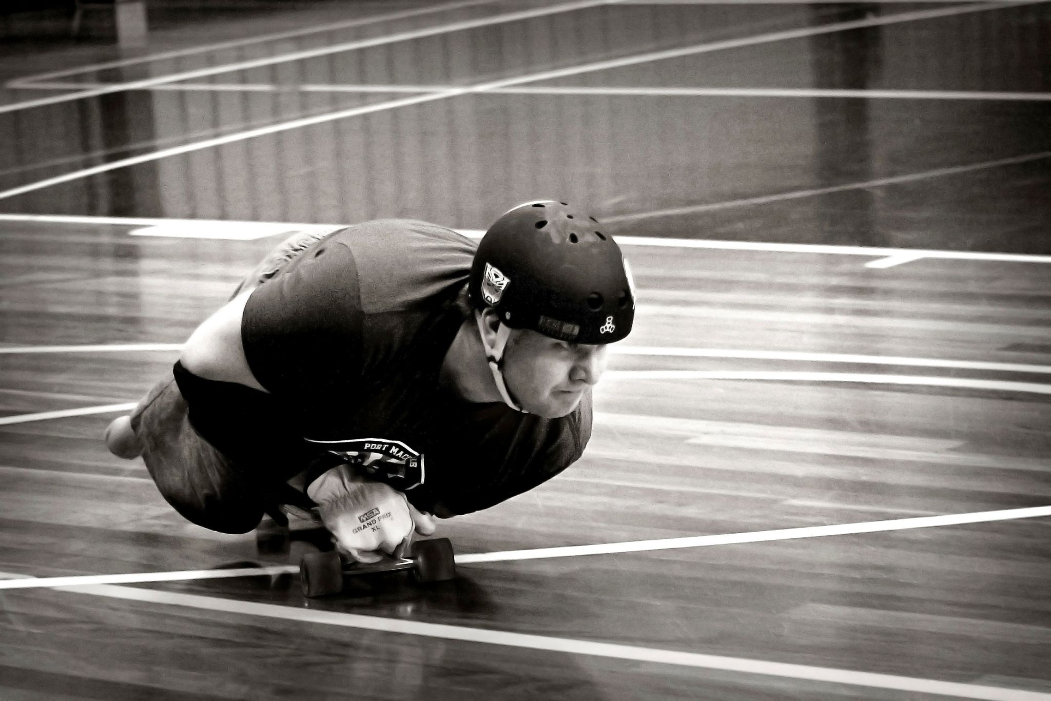 A man with no legs and one arm on a skateboard on a wood floor painted with basketball stadium lines, greyscale.
