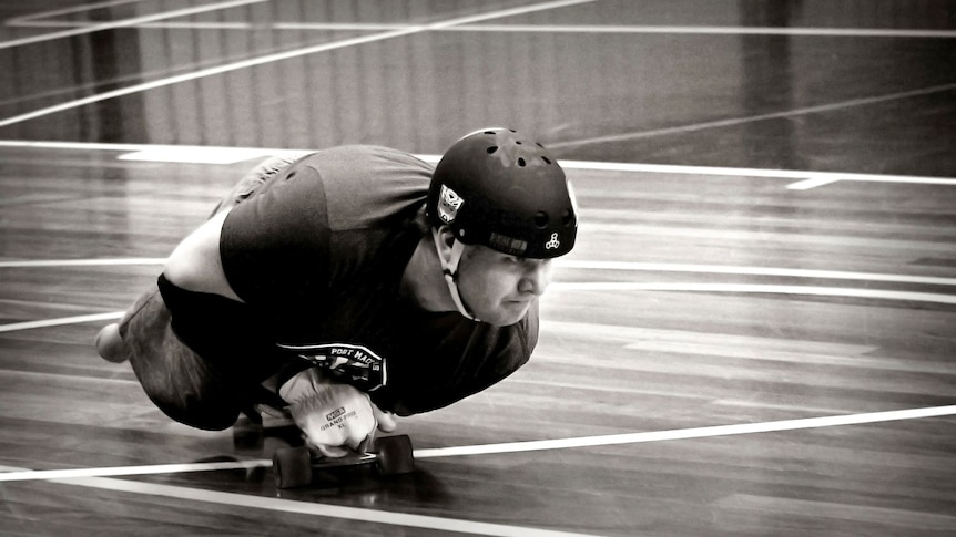 A man with no legs and one arm on a skateboard on a wood floor painted with basketball stadium lines, greyscale.