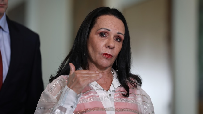 Burney gestures with her hand and looks serious while standing inside parliament.