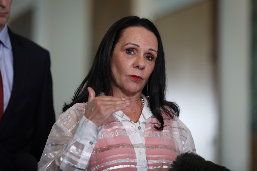 Burney gestures with her hand and looks serious while standing inside parliament.