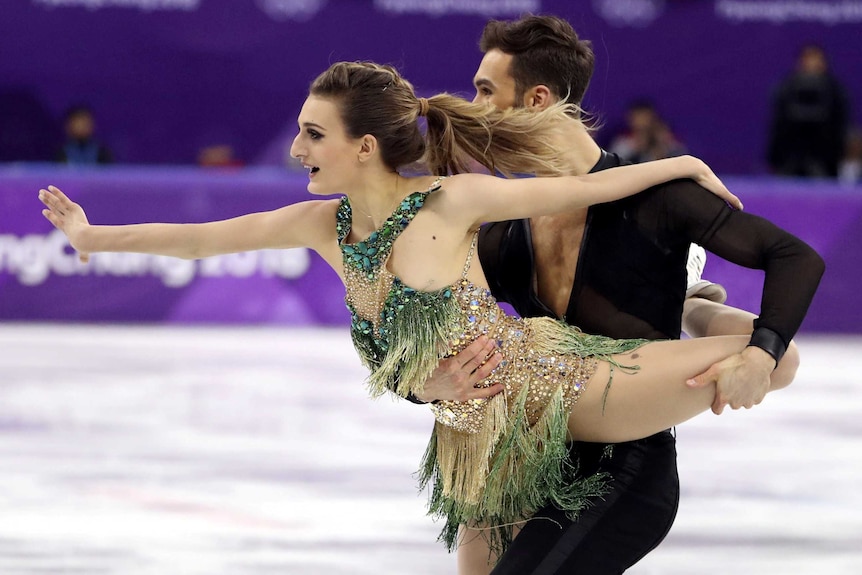 Guillaume Cizeron holds Gabriella Papadakis in front of him as they skate, her arm outstretches, the strap of her dress undone