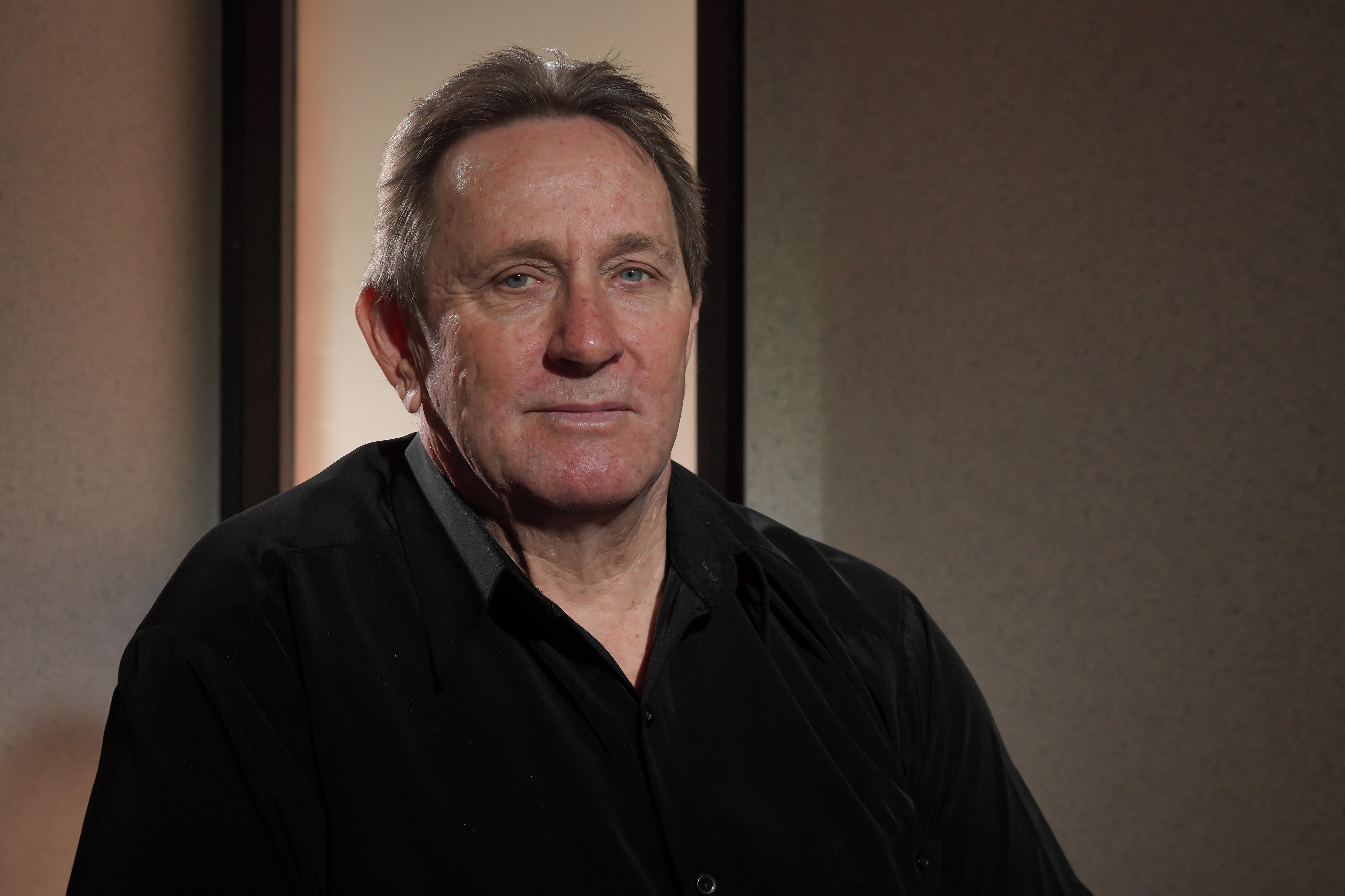 A middle-aged man in a black shirt, sitting. 