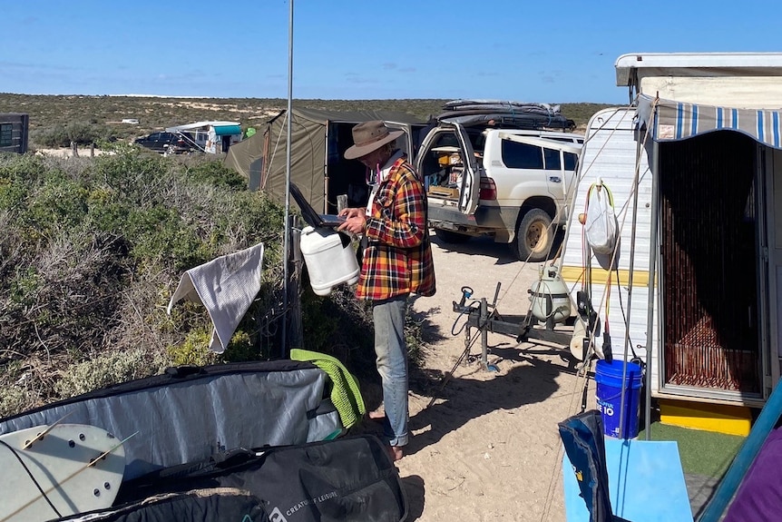 A student in an outback area, near a caravan, and looking at research on a laptop.