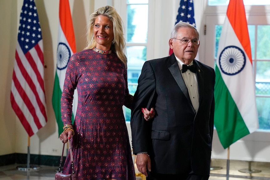Nadine and Bob Menendez, dressed in formal wear, walk past American and Indian flags.