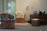 Two wicker chairs inside a house with white walls. There is also a table and a phone mounted on the wall.