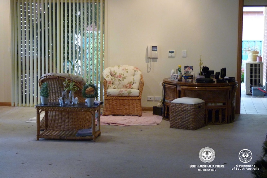 Two wicker chairs inside a house with white walls. There is also a table and a phone mounted on the wall.