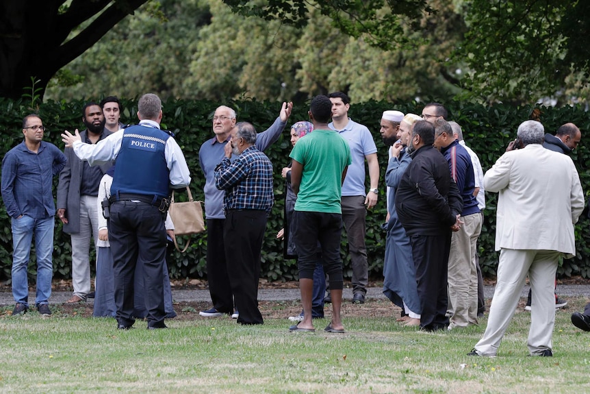 Police talk to a group of witnesses on a sidewalk near a mosque.