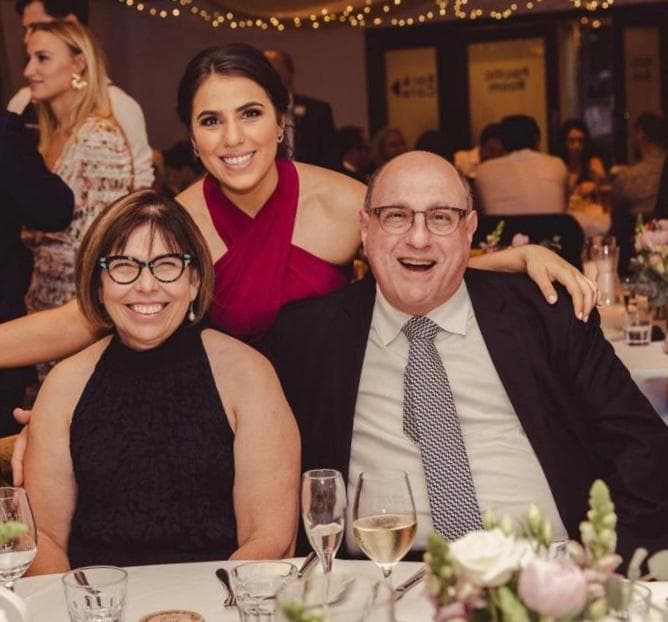 公式の場で、笑顔で座る両親の後ろに立つ娘さん。