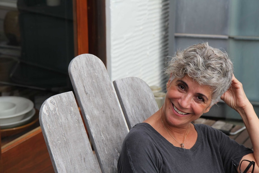 Woman smiles sitting outside on a wooden chair.