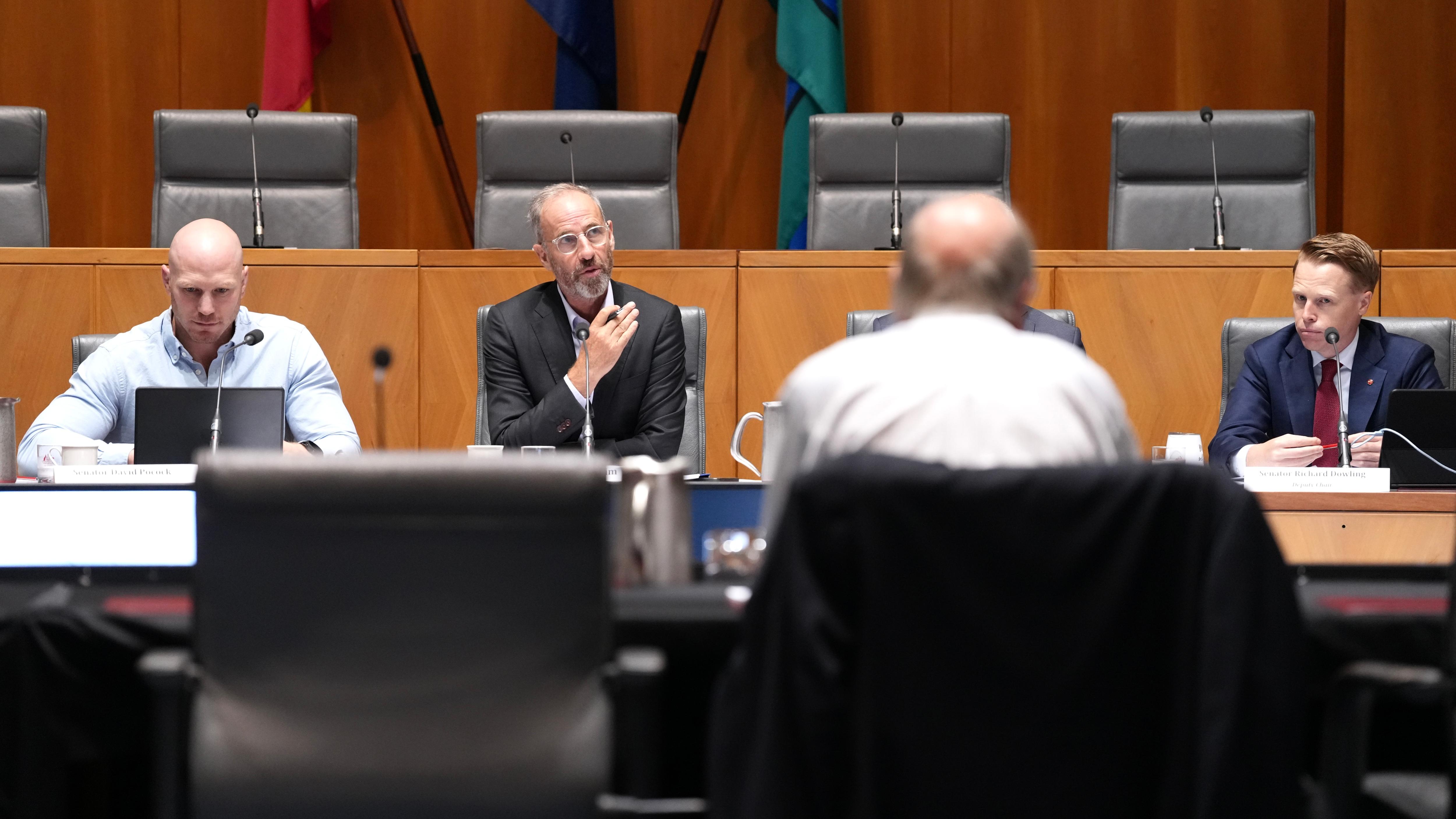 Los senadores se sientan en un escritorio, Bernie Fraser les da la espalda.