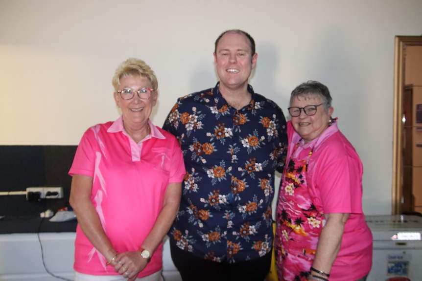 A man with a pattern shirt standing next to two women wearing pink