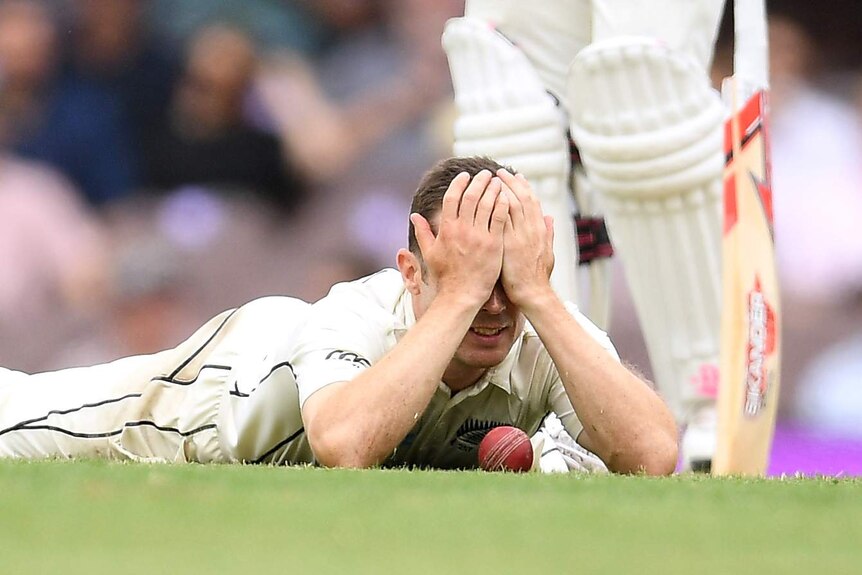 Todd Astle covers his eyes with his hands as he lies on the ground with a cricket ball on the floor between his elbows