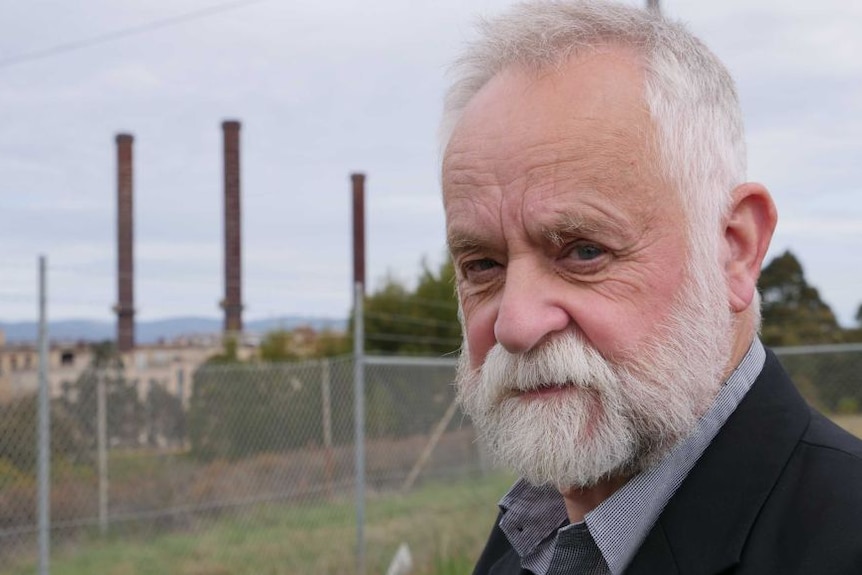 A man with a beard looks at the camera with a power station in the background