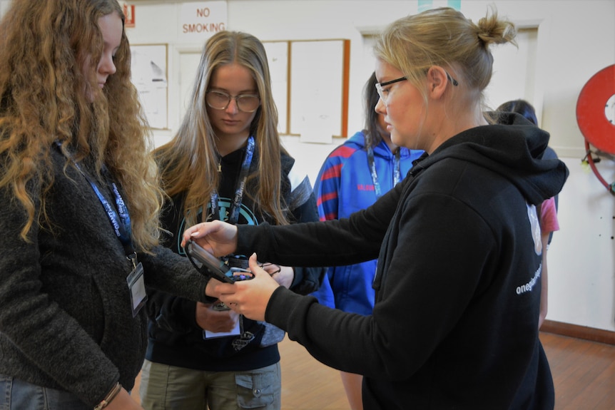 Girl with short blonde hair teaching other girls to use technology.