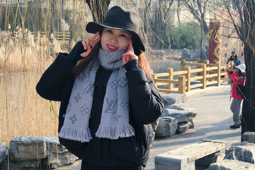 A woman in a black jacket while wearing a grey scarf in a park.