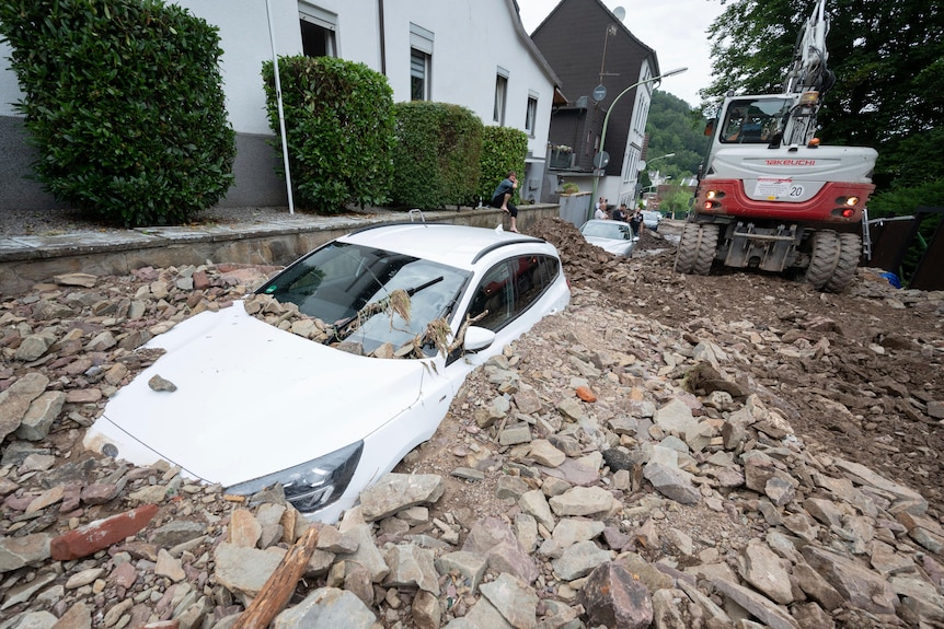 A car semi-submerged in rubble in a street in a German village.