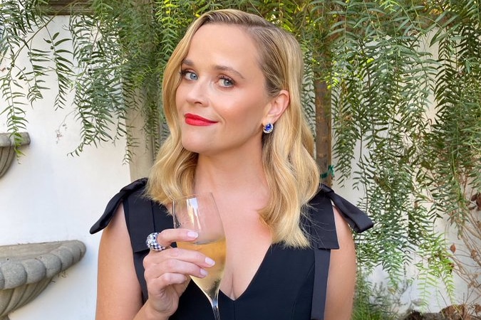 Reece Witherspoon is wearing a black dress and holding a glass of wine