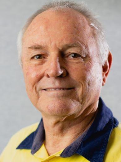 An older man with grey hair and a receding hairline smiles