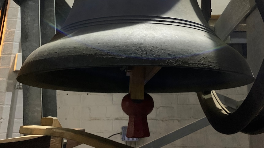 A steel bell, roughly the size of a person, hanging in a church bell tower