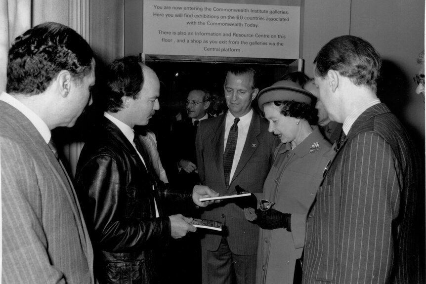 A black and white photo of Philip Salom presenting his book to the Queen 