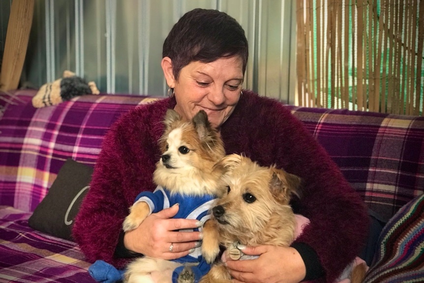A woman wearing a red and purple jumper holding two dogs, smiling at them