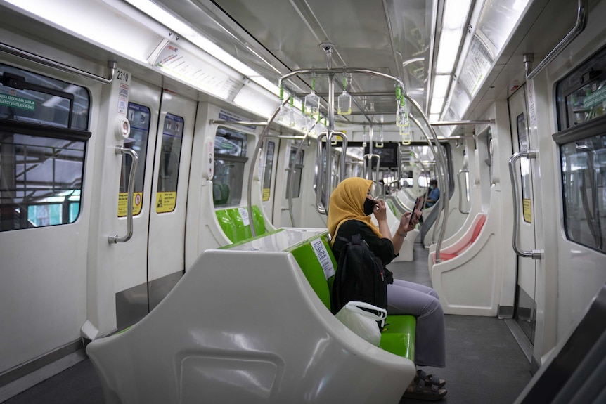 A woman wearing a protective mask uses her phone in a Light Rail Transit train in KL.