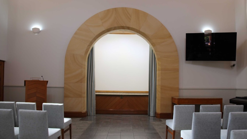 Interior of chapel at a cemetery in Sydney with seats facing a podium and an archway at the front