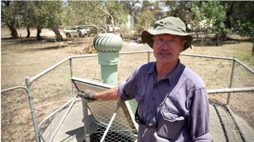 A man stands in front of an underground bunker on a rural property.